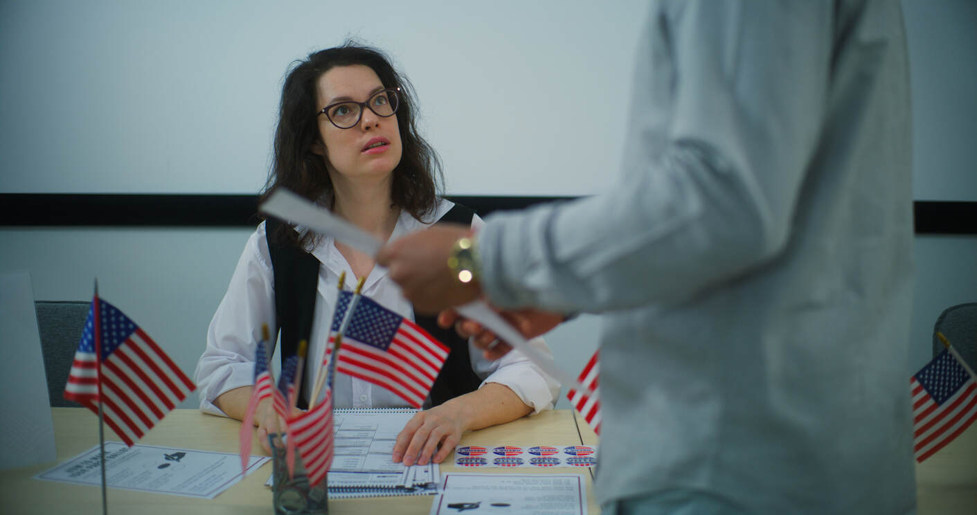 Person at a desk with American flags looking at an applicant, representing a USCIS I-485 interview – learn why applications are flagged and how to prepare.